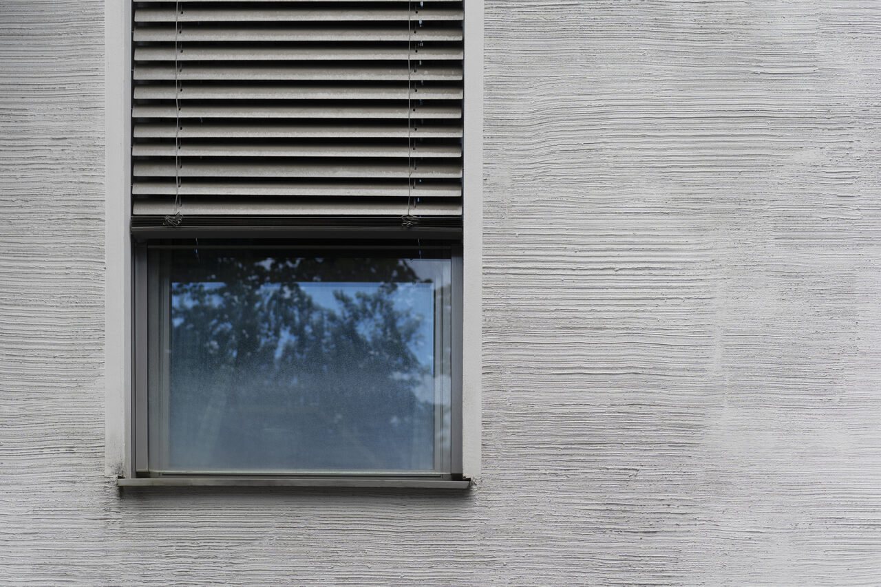 Fenster mit heruntergelassenem Außenrollladen an einer grauen Fassade